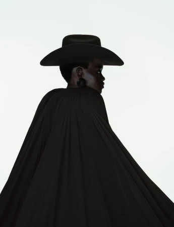 Model Caren Jepkemei wearing a black hat and pleated black cape against a white background for 10 Magazine