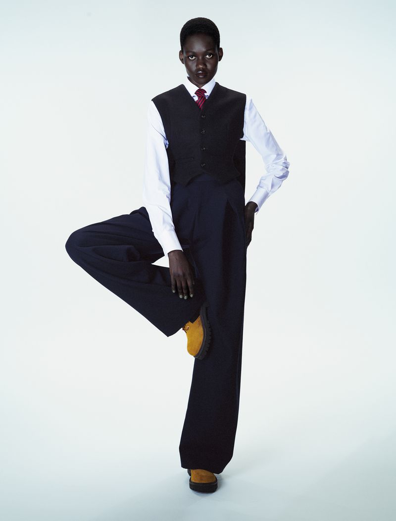 Model Caren Jepkemei balancing on one leg in a dark vest and trousers for a 10 Magazine editorial by Ferry van der Nat.