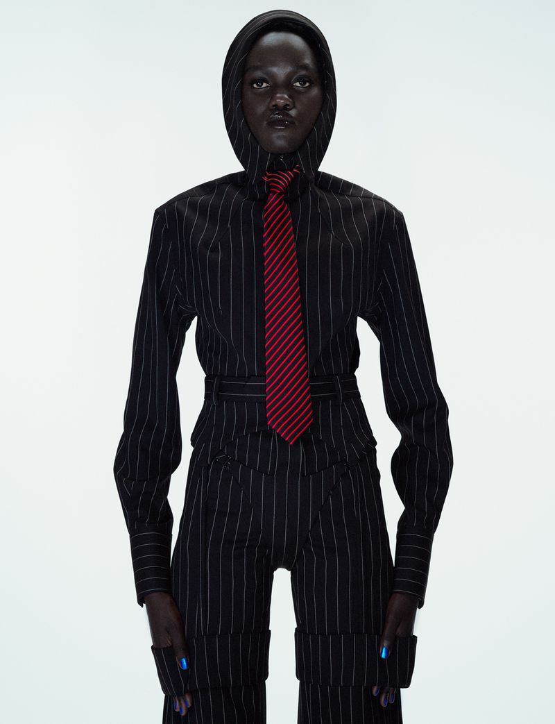 Model Caren Jepkemei in a pinstripe hooded top and matching trousers with a red tie against white background