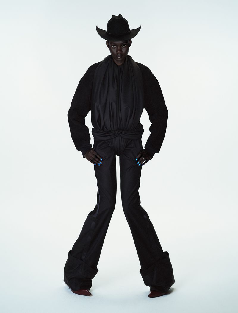 Model Caren Jepkemei in all-black attire including a cowboy hat and flared trousers against a plain white studio background.