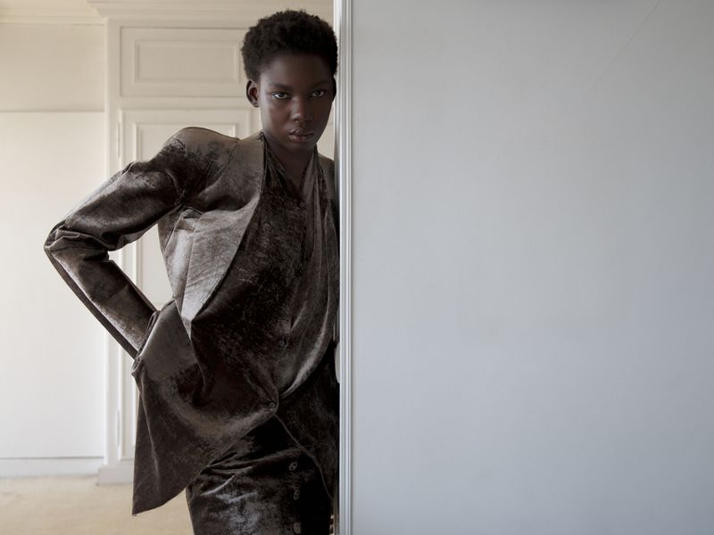 Black woman wearing a dark velvet blazer leaning against a white door frame in an interior setting