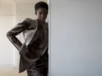 Black woman wearing a dark velvet blazer leaning against a white door frame in an interior setting