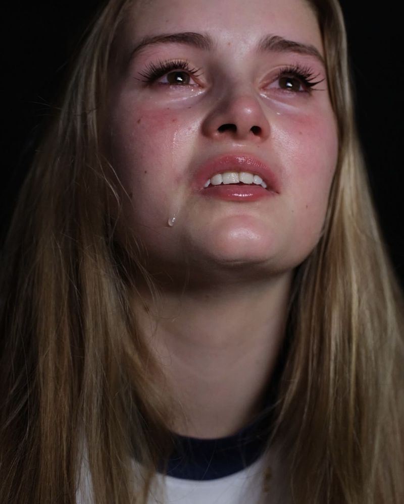 Close-up portrait of a young blond woman crying with tears streaming down her face against a dark background