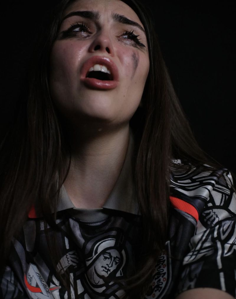 Close-up portrait of a woman with smudged makeup and dark hair crying against a dark background