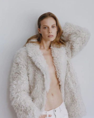 Model in a textured cream fuzzy jacket and white trousers posing against a pale background