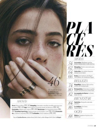 Close-up portrait of a woman holding her hand near her face, wearing two textured rings and showcasing natural freckles.