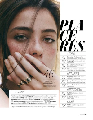 Close-up portrait of a woman holding her hand near her face, wearing two textured rings and showcasing natural freckles.