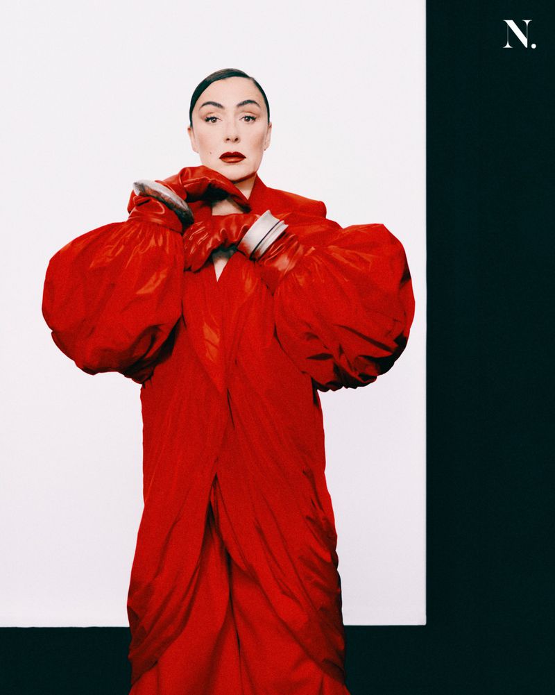 Model wearing a vibrant red coat and matching red leather gloves against a split white and black background
