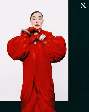 Model wearing a vibrant red coat and matching red leather gloves against a split white and black background