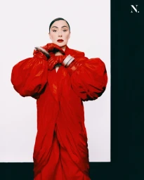 Model wearing a vibrant red coat and matching red leather gloves against a split white and black background