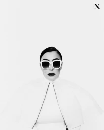 Monochrome portrait of a person wearing white sunglasses and a structured white jacket against a plain background
