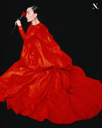 Woman in a long red dress holding a red rose against a plain black background for Noir Magazine