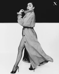 Model in long belted trench coat posing against a split black and white background for Noir Magazine editorial.