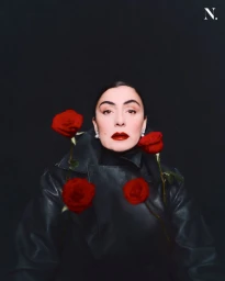 Woman in dark leather jacket surrounded by four red roses against a dark background for Noir Magazine editorial.