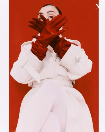 Model in white coat and red leather gloves covering her face against a red background for Noir Magazine Full circle editorial.