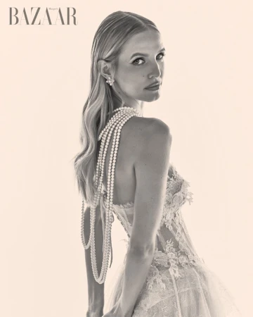 Portrait of a blonde woman wearing a lace gown and layered pearl necklaces against a neutral seamless backdrop for Harper's Bazaar