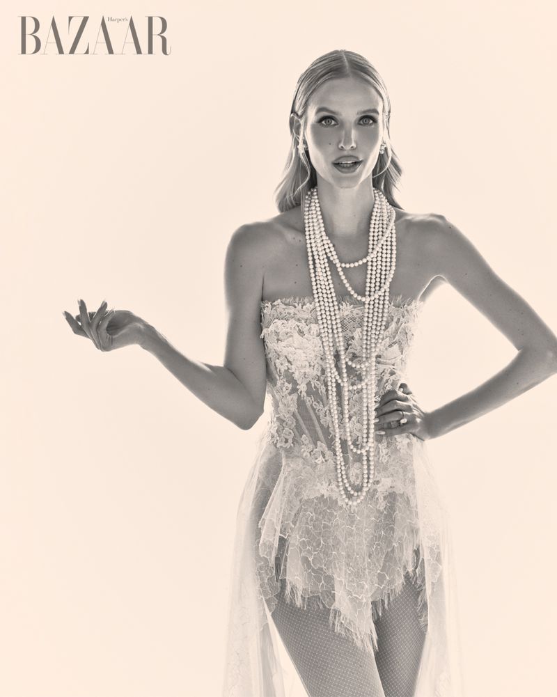 Monochrome fashion editorial portrait of a woman wearing a strapless lace dress and layered pearl necklaces.