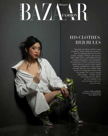 Woman in an oversized white shirt and metallic boots posing against a dark grey corner backdrop for Harper's Bazaar Vietnam.