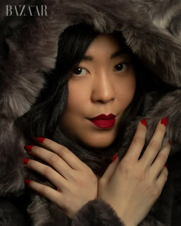 Close-up portrait of a woman wearing a furry grey hooded coat with bold red lipstick and manicured red nails