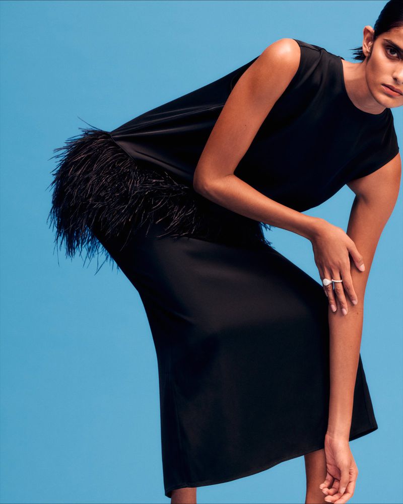 Model in a black feather-trimmed dress posing against a vibrant blue studio backdrop for Liberty curation