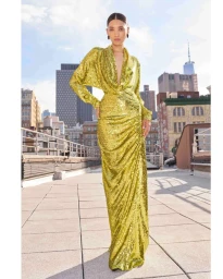 Model wearing a shimmering gold sequined long-sleeve gown standing on a city rooftop with skyscrapers.