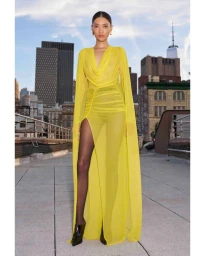 Model wearing a sheer yellow hooded cape gown on a rooftop with city skyline backdrop