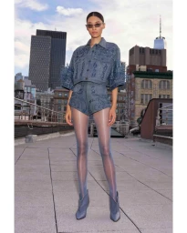 Model wearing an embellished blue denim set and matching tights on a rooftop overlooking city skyscrapers.