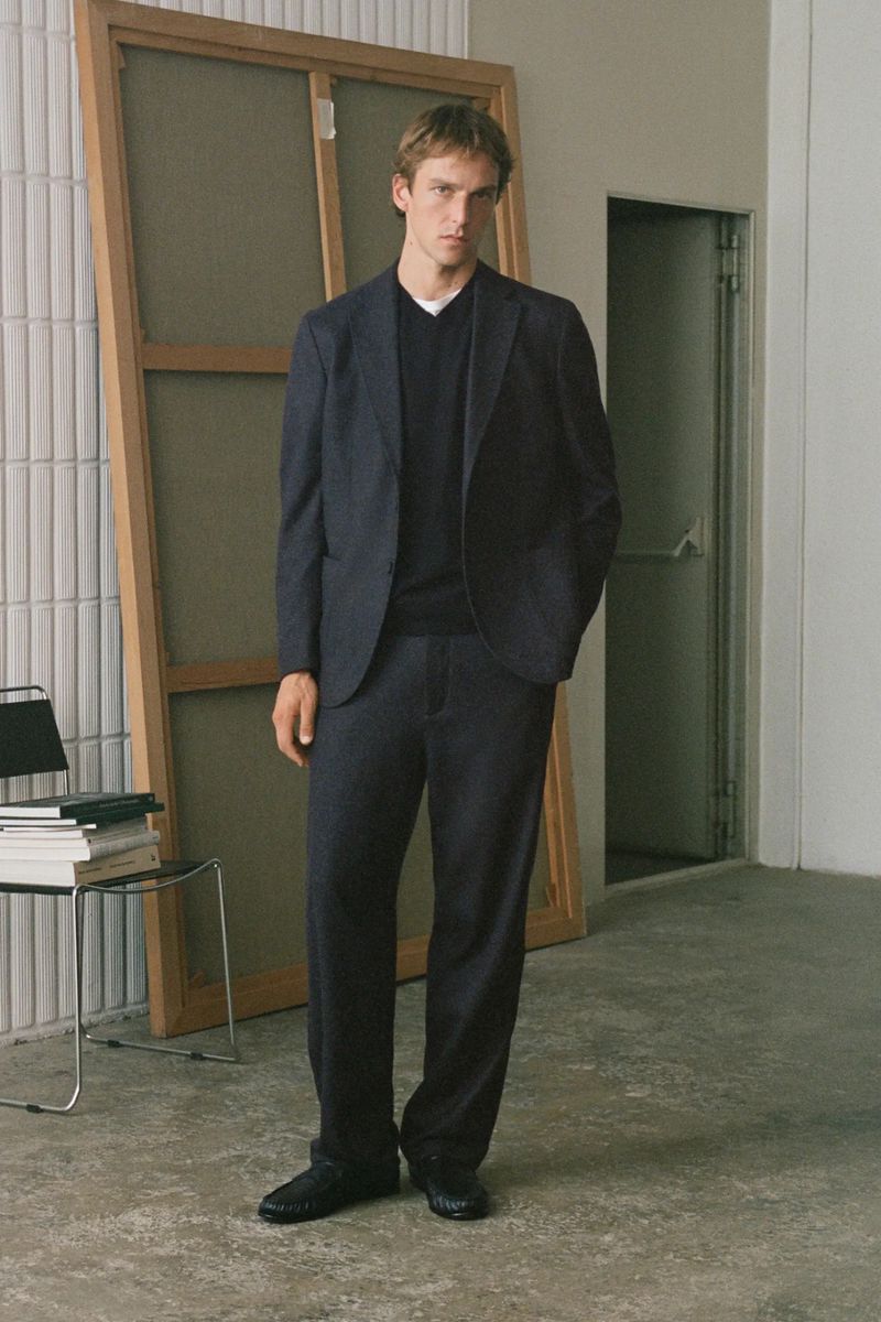 Man wearing a dark suit and V-neck sweater standing in an interior space with a large framed canvas.