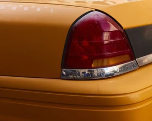 Close-up of a yellow taxi tail light and rear body panel with a reflective chrome trim piece