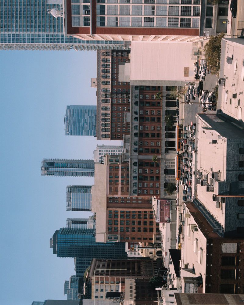 High-angle view of urban cityscape with diverse architectural buildings and parked vehicles under clear daytime sky