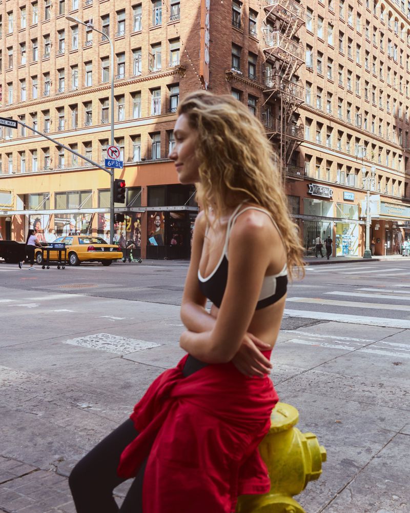 Woman with long blonde wavy hair sitting on a yellow fire hydrant on a city street wearing activewear