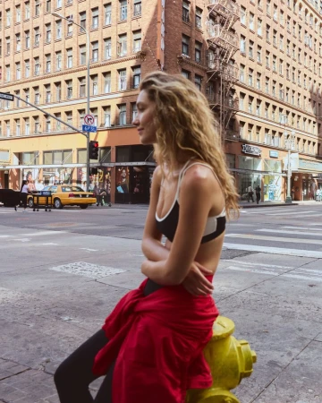 Woman with long blonde wavy hair sitting on a yellow fire hydrant on a city street wearing activewear