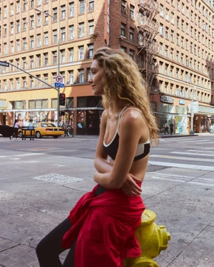 Woman with long blonde wavy hair sitting on a yellow fire hydrant on a city street wearing activewear