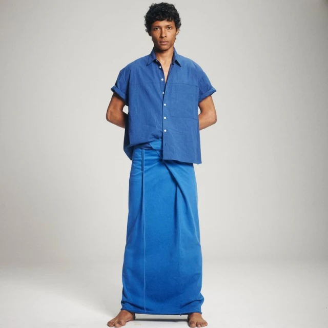 Full shot of a person in a royal blue button-down shirt and matching sarong-style wrap standing against a neutral studio backdrop.