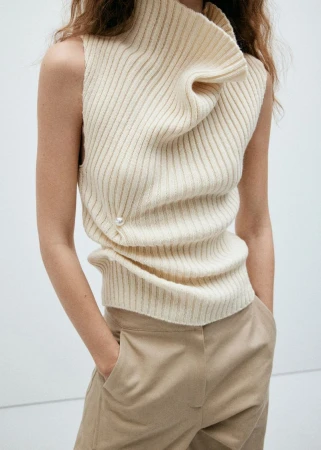 Model wearing a ribbed cream high neck sleeveless top and beige trousers against a plain white background