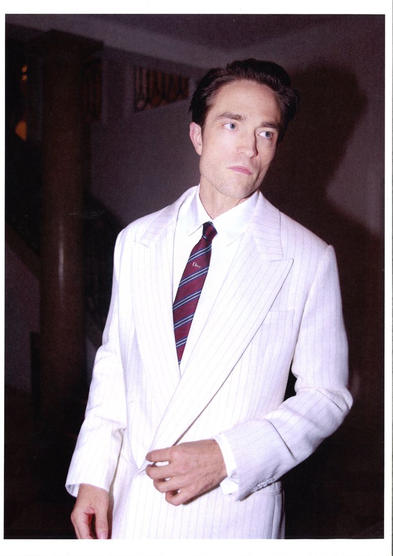 Robert Pattinson wearing a white pinstripe suit and striped tie against an interior background for Dior