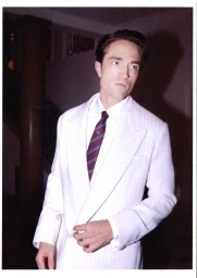 Robert Pattinson wearing a white pinstripe suit and striped tie against an interior background for Dior