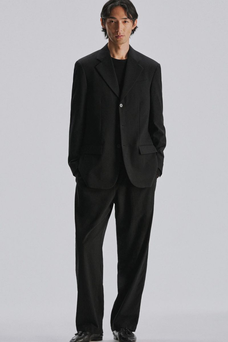 Model Naoki Sumiya wearing a black suit and trousers against a neutral grey studio backdrop