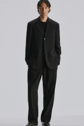 Model Naoki Sumiya wearing a black suit and trousers against a neutral grey studio backdrop