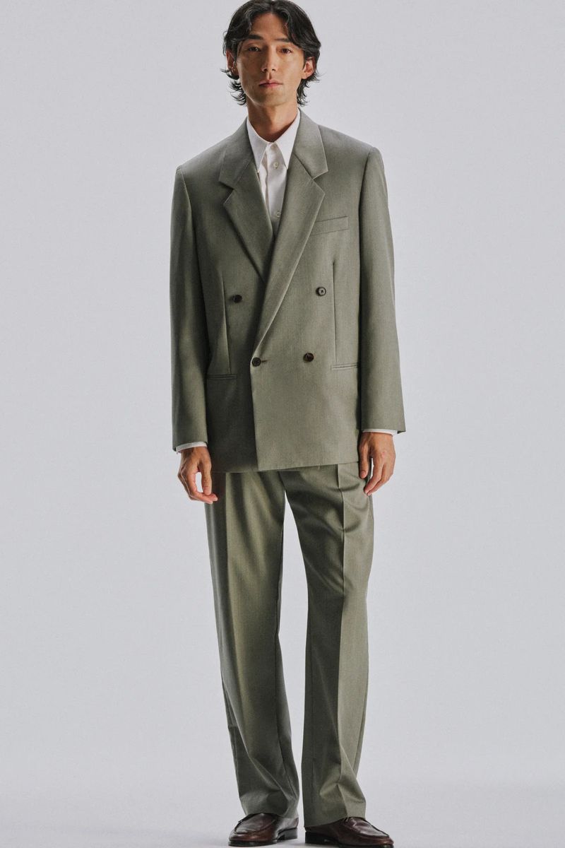 Model Naoki Sumiya in a sage green double-breasted suit against a light grey seamless studio backdrop for The Row.