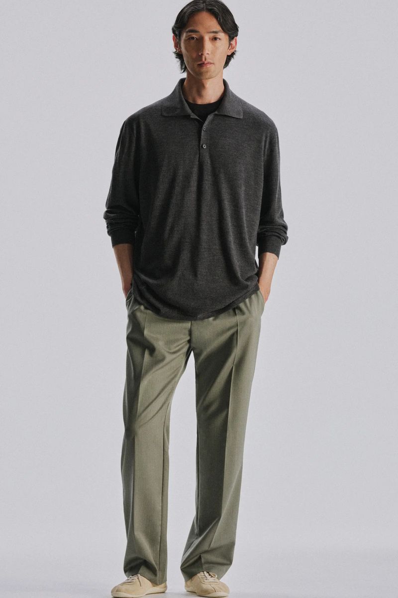 Male model wearing a dark grey polo shirt and olive trousers standing against a white seamless background