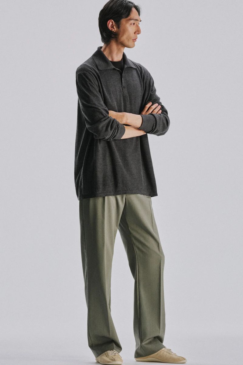 Model with arms crossed wearing a dark grey polo shirt and olive trousers against a plain white background