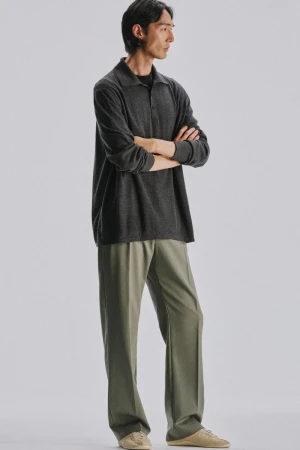 Model with arms crossed wearing a dark grey polo shirt and olive trousers against a plain white background