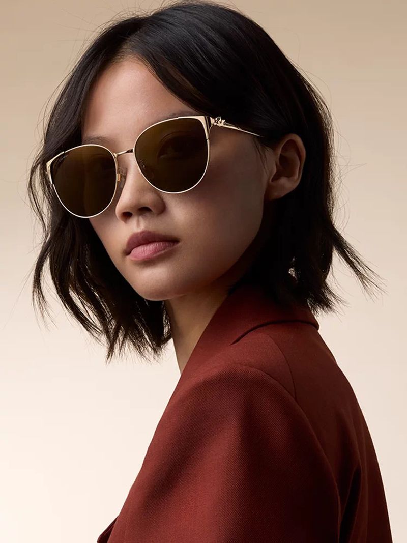 Model wearing gold-framed sunglasses and a rust blazer against a neutral backdrop for Cartier Panthère de Cartier campaign.