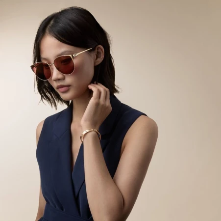 Model wearing gold sunglasses and a gold bracelet with a navy sleeveless vest top against a neutral background.