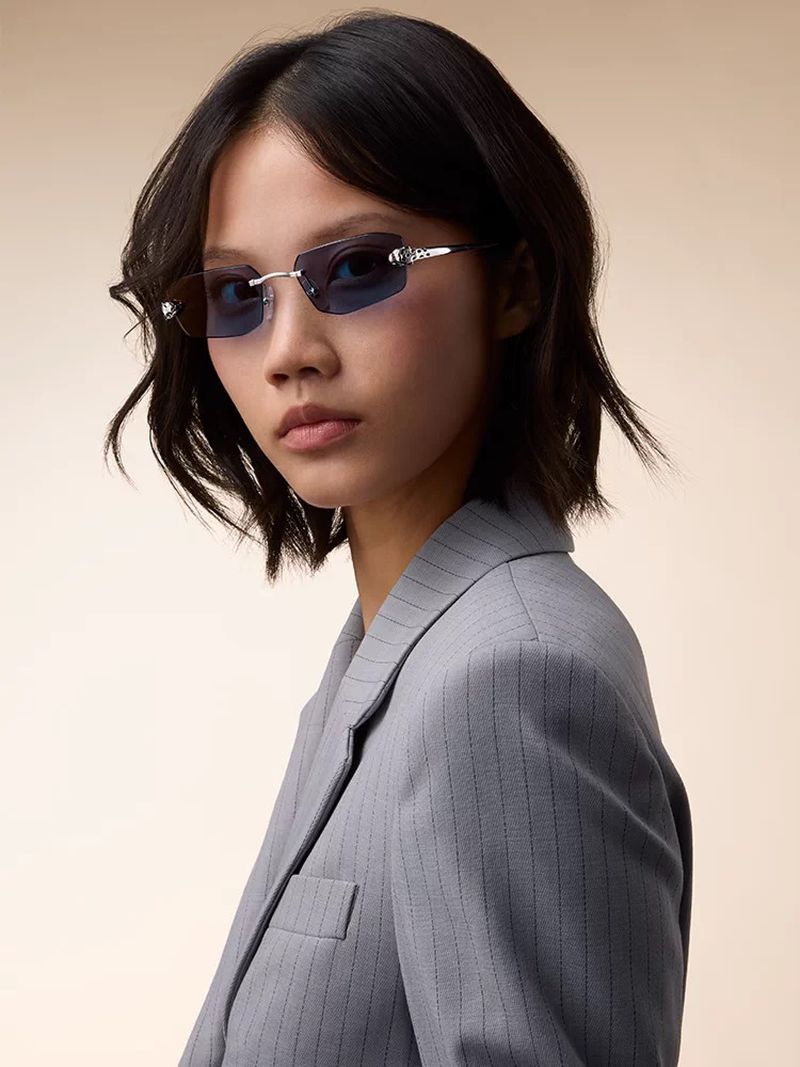 Model wearing blue-tinted rimless sunglasses and a grey pinstripe blazer against a neutral backdrop for Cartier.