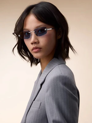 Model wearing blue-tinted rimless sunglasses and a grey pinstripe blazer against a neutral backdrop for Cartier.