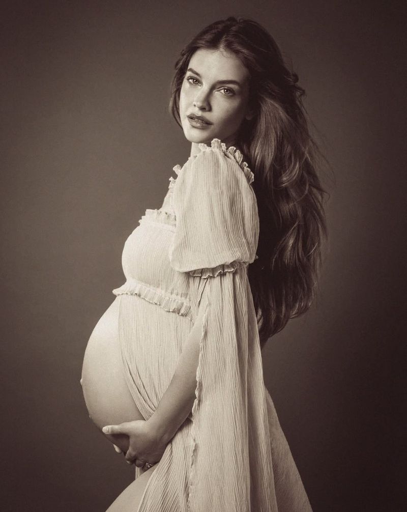 Barbara Palvin in a white vintage dress posing in profile against a dark background for Victoria's Secret