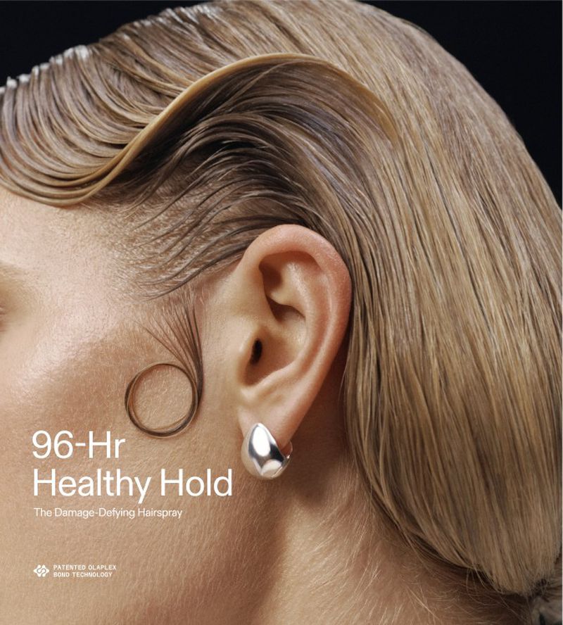 Close-up portrait of a woman with sculpted blonde hair, a circular baby hair curl on her cheek, and a silver earring.