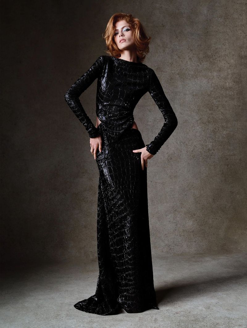 Model with red hair wearing a long black sequined dress against a textured grey background